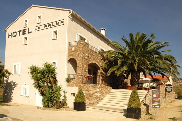 A two-story building with a sign reading "HOTEL LA PALMA" and a stone facade. - Hôtel La Palma (Patrimonio)