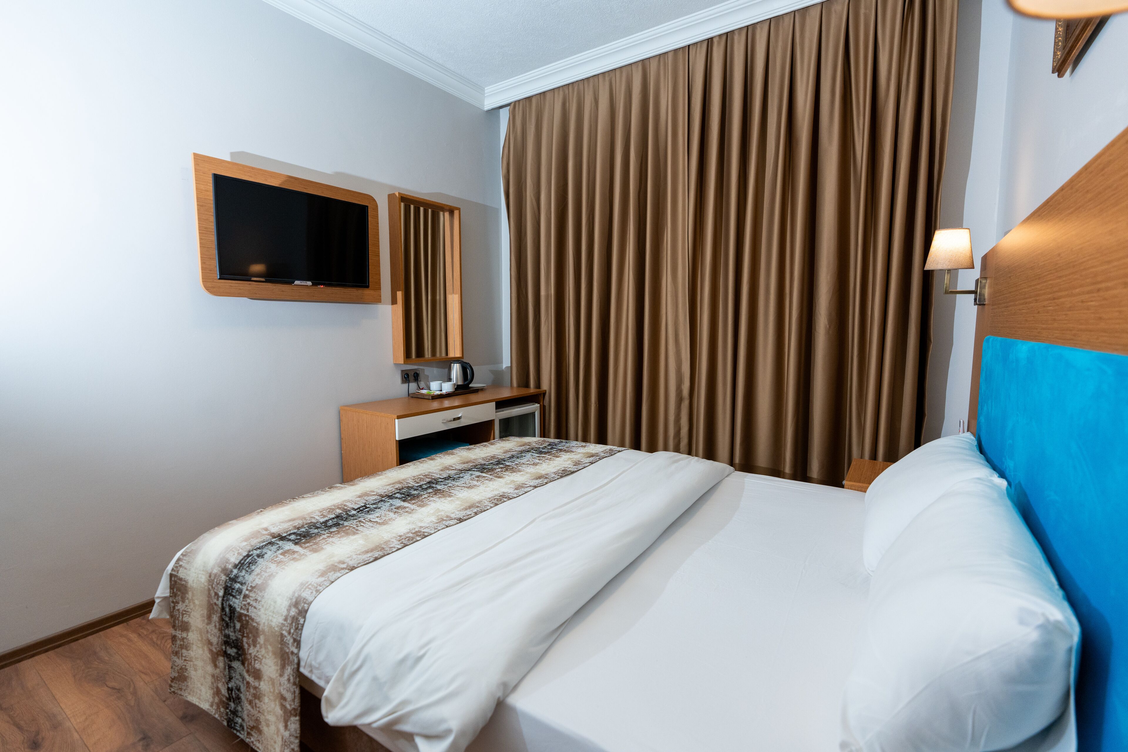 A hotel room with a bed, a television, a desk, and a window with curtains.