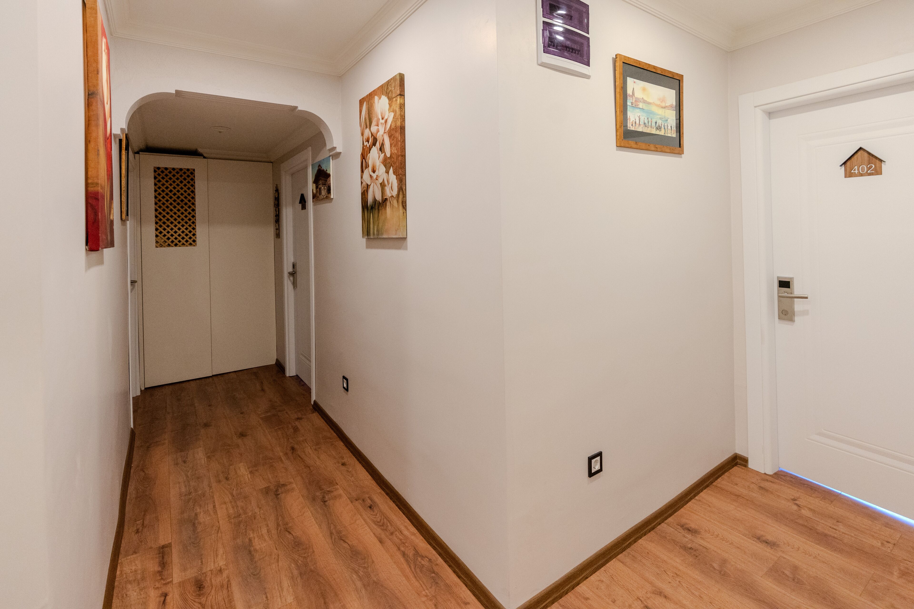 Un pasillo con piso de madera, paredes blancas y una puerta con el número 402.