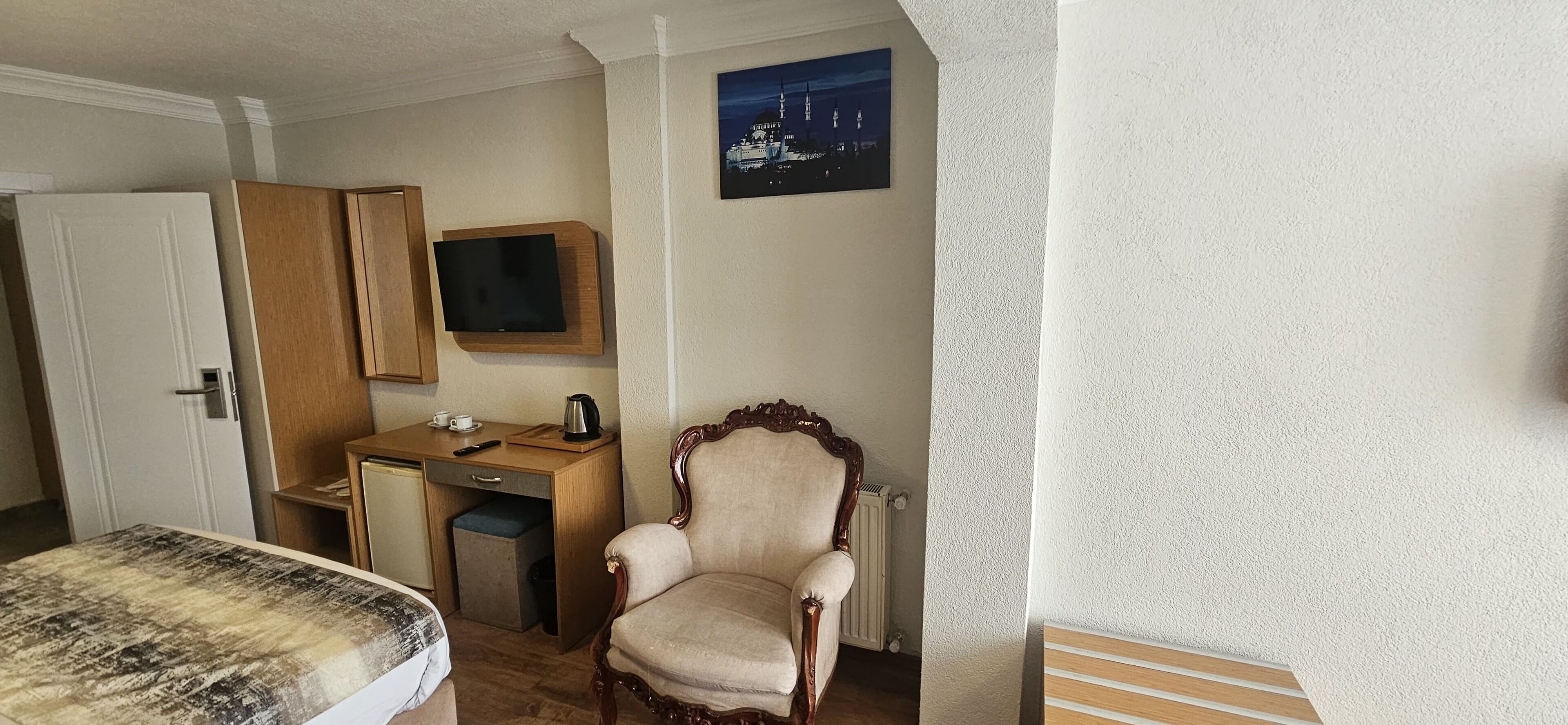 A room with a bed, a wooden desk with a television, a chair, and a radiator.
