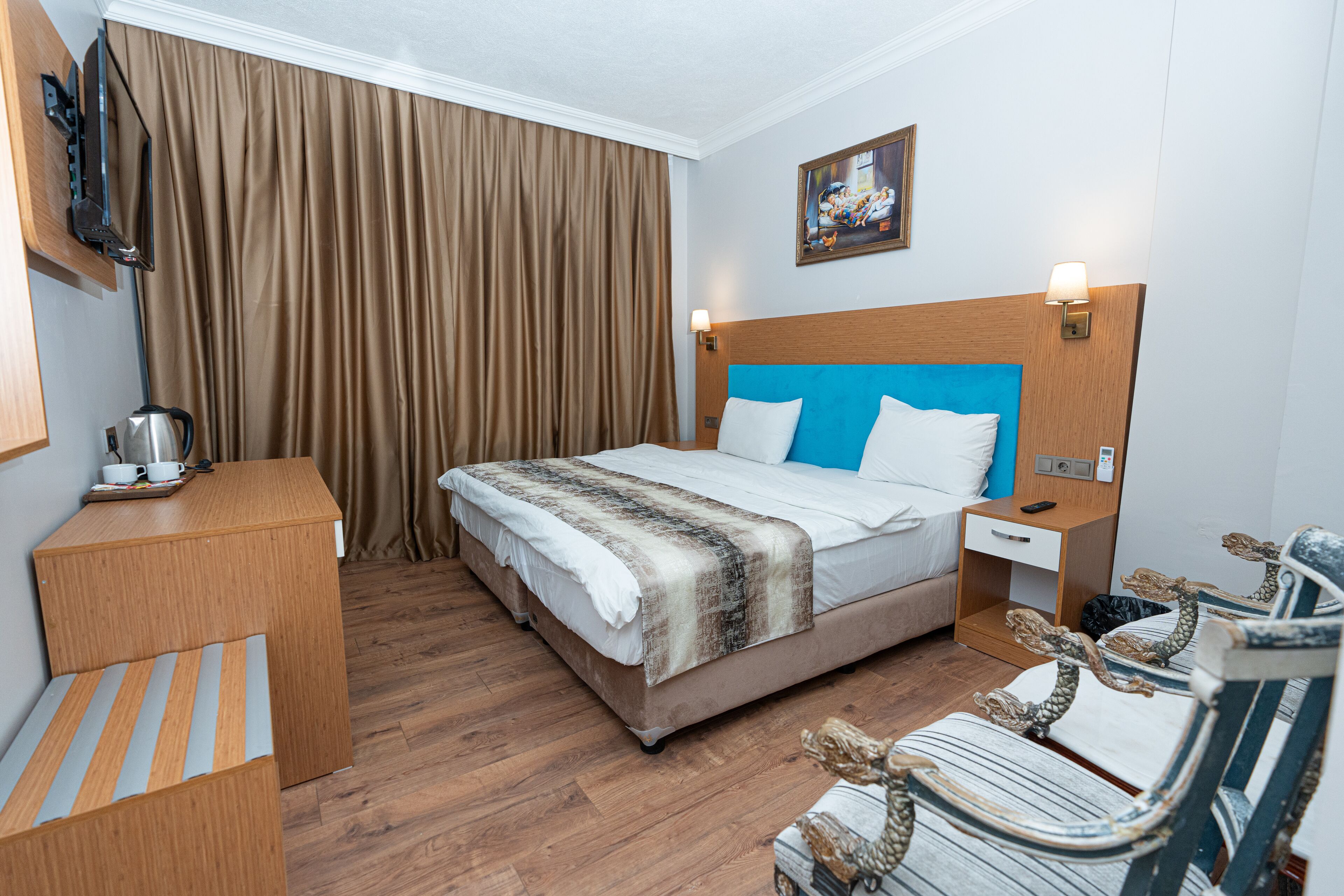 Habitación de hotel con cama, escritorio, silla, mesita de noche, lámpara y televisor.