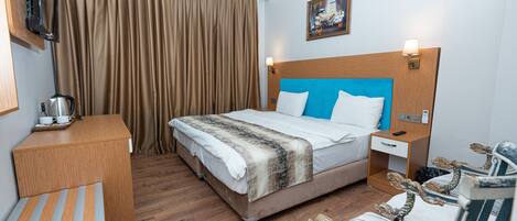Habitación de hotel con cama, escritorio, silla, mesita de noche, lámpara y televisor.