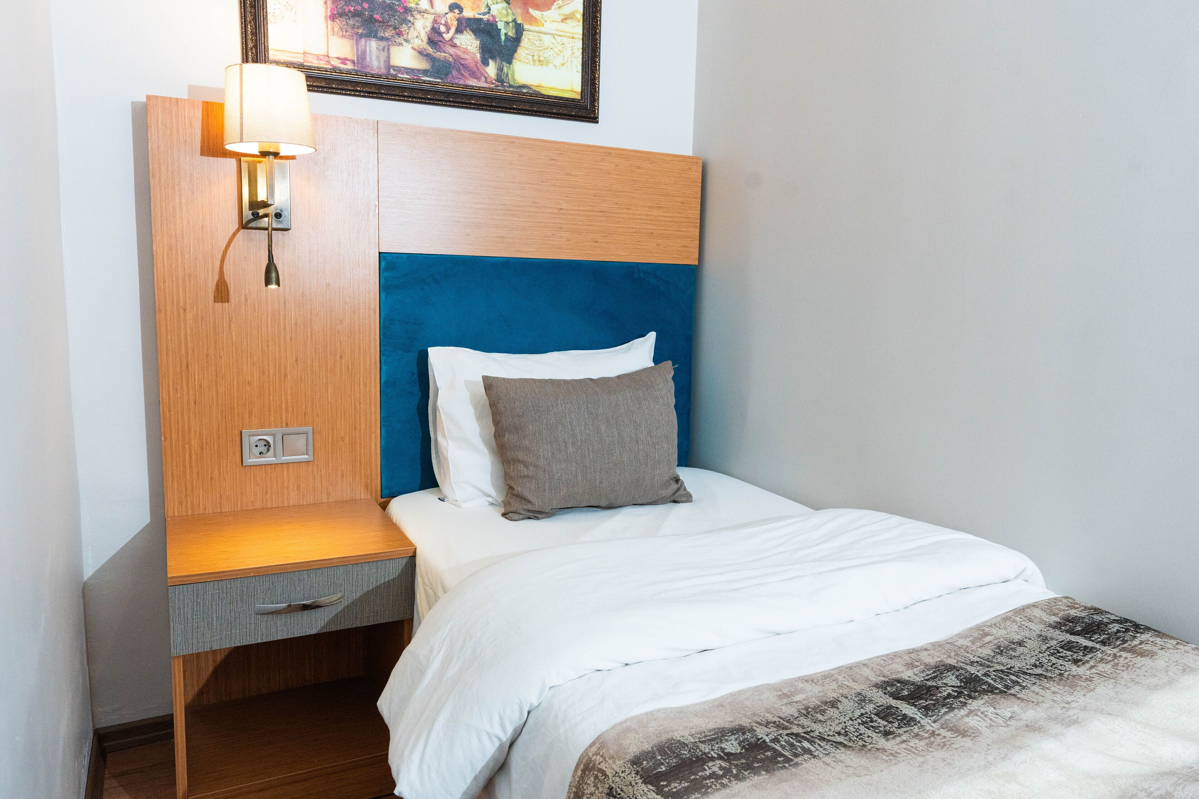 Un lit bien fait, avec une tête de lit bleue, une lampe de chevet et une petite table de nuit en bois dotée d’un tiroir.