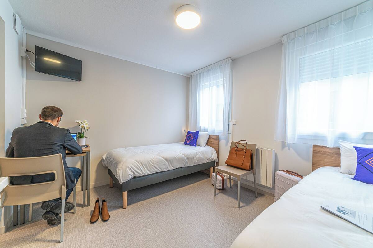 A hotel room with a bed, a desk with a computer, a chair, and a TV mounted on the wall.
