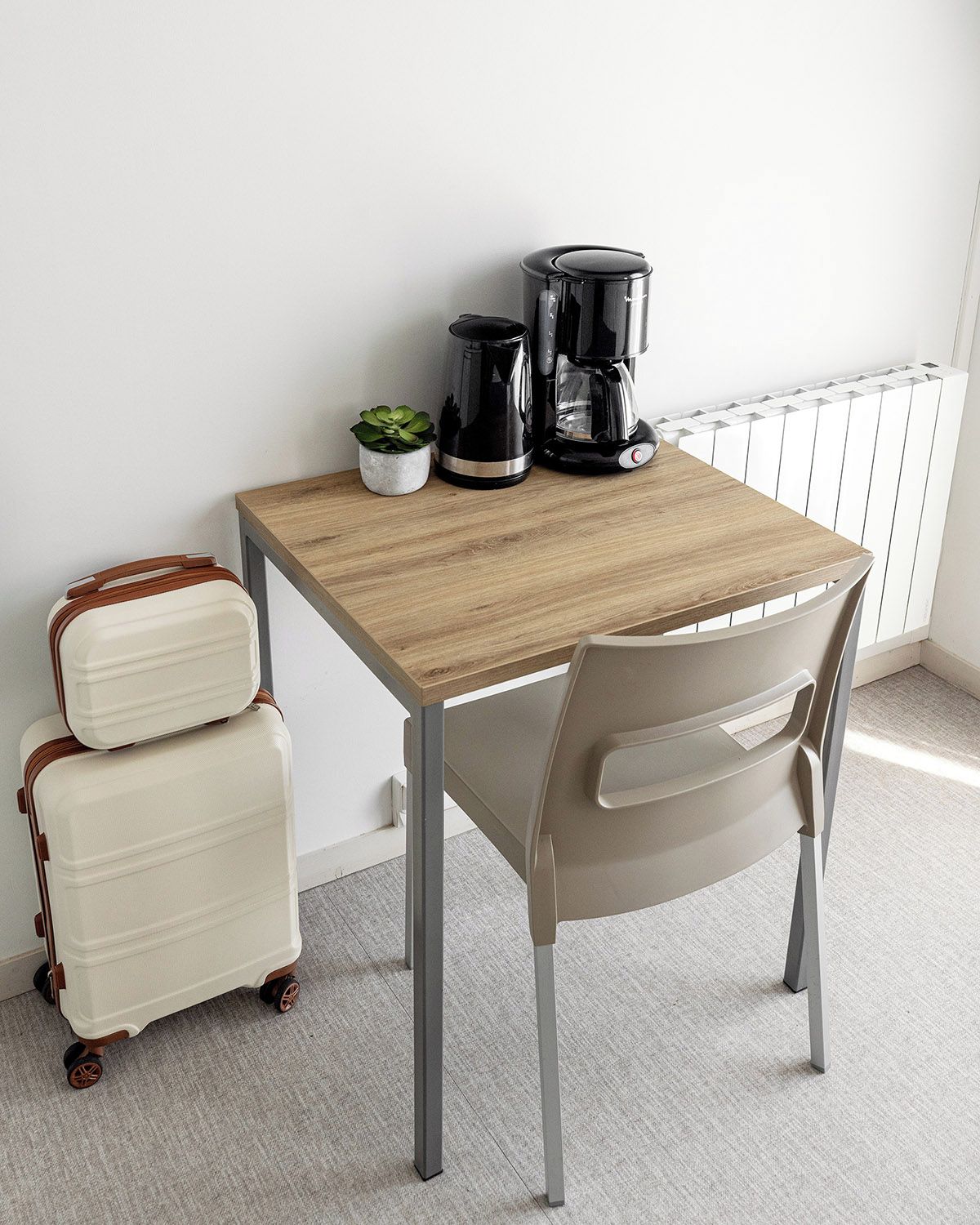 A small room with a wooden table, a chair, a radiator, and a suitcase.