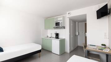 A compact hotel room with a kitchenette, a bed, a desk with a laptop, and a TV.