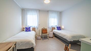 A twin bedroom with two beds, a desk, a chair, and a suitcase.
