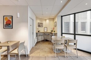 A modern office space with a long table, chairs, and a large window with a view of buildings. - Montempô Apparthôtel Lyon Sud (Venissieux)
