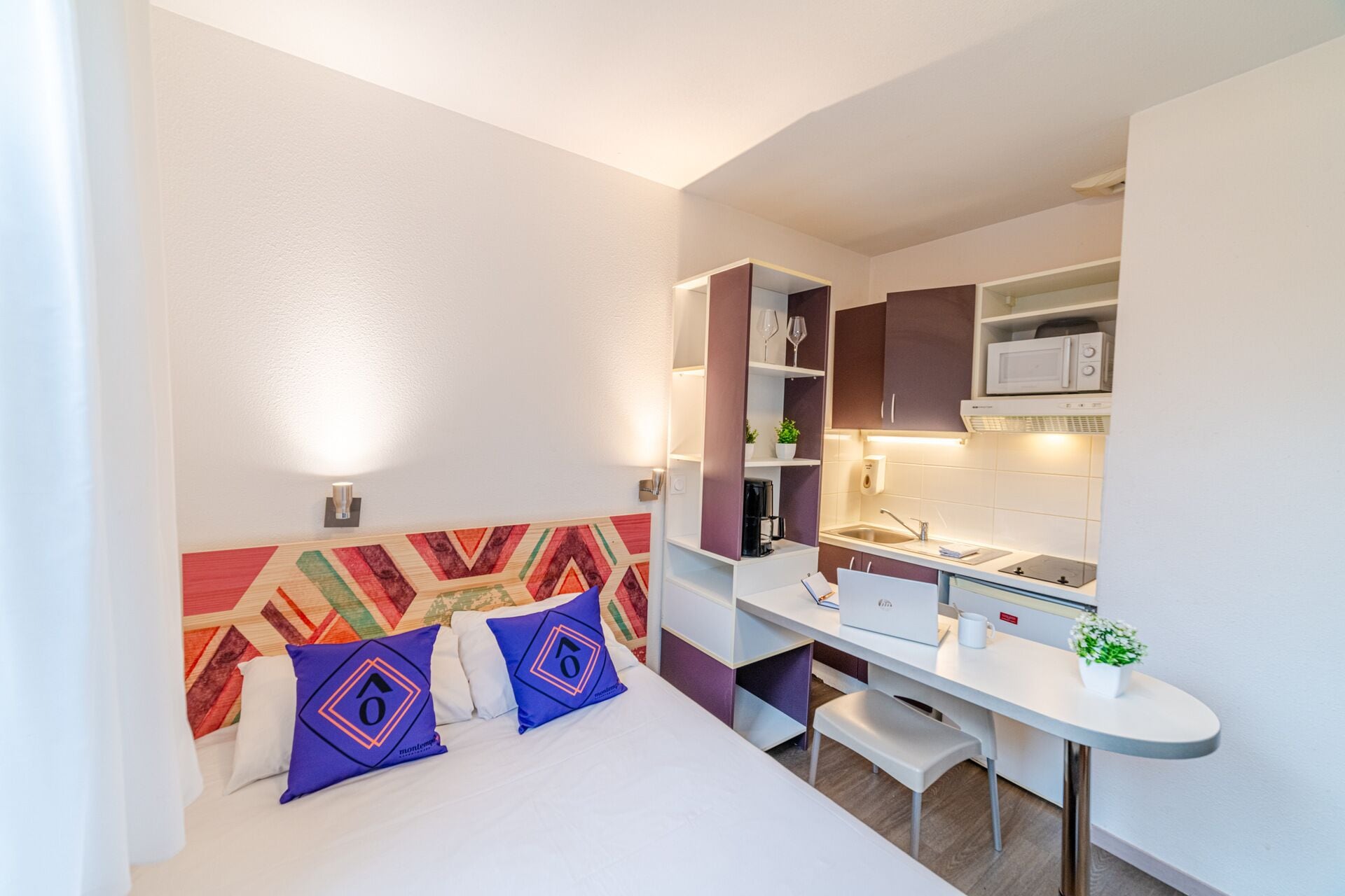 A compact hotel room with a bed, a desk, and a kitchenette.