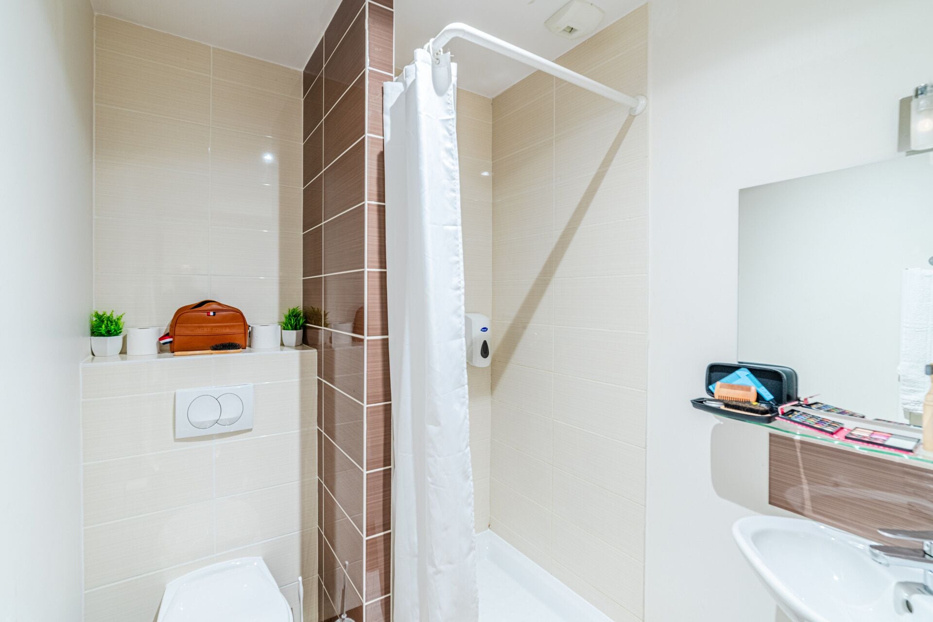 A modern bathroom with a shower, toilet, and sink. There is a towel rack, a small plant, and a toiletry bag on the counter.