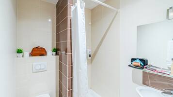 A modern bathroom with a shower, toilet, and sink. There is a towel rack, a small plant, and a toiletry bag on the counter.