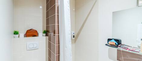 Un baño moderno con ducha, inodoro y lavabo. Hay un perchero, una planta pequeña y un neceser sobre la encimera.