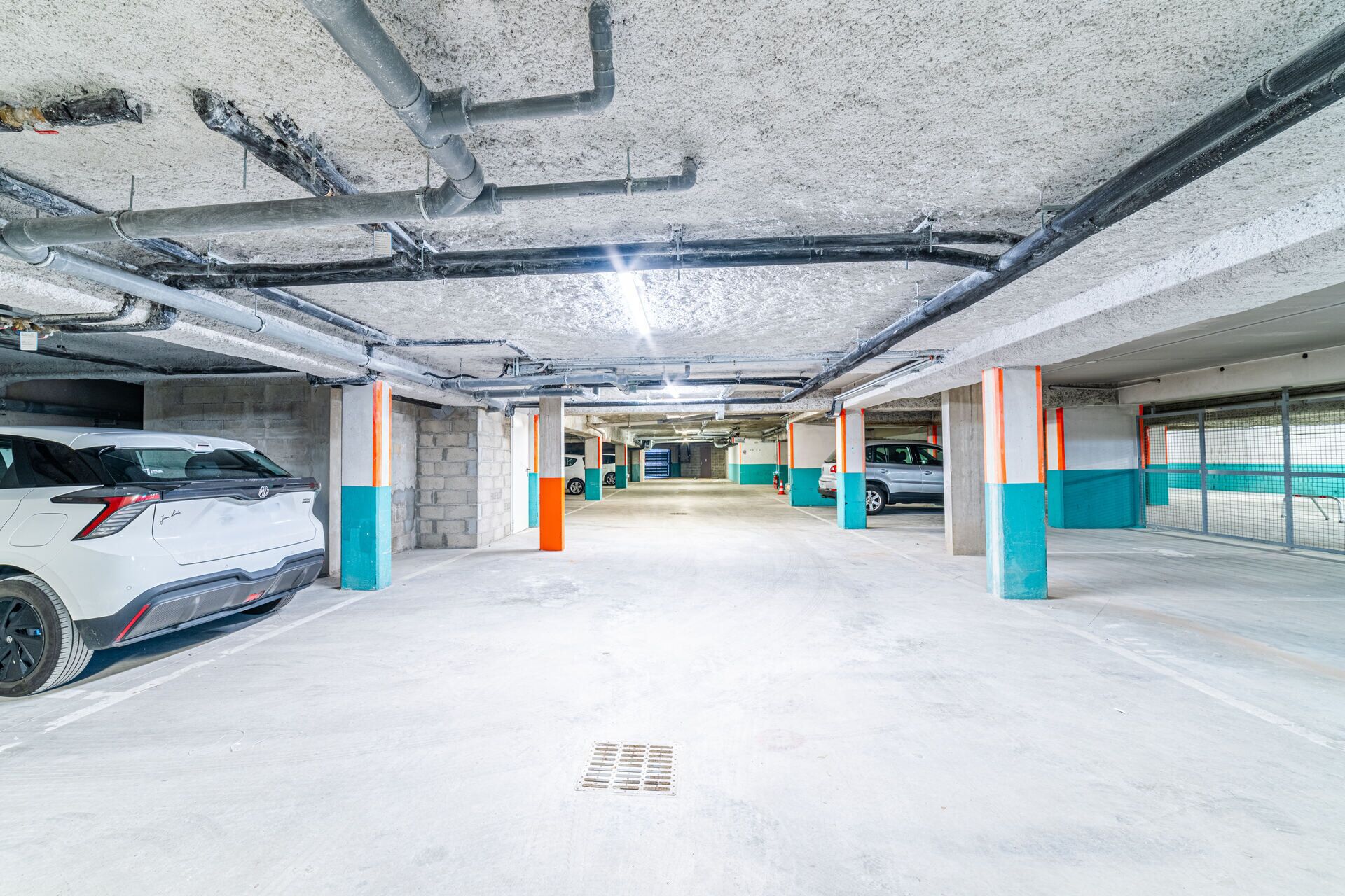 Uma garagem de estacionamento com vários níveis, pilares de concreto e tubulações suspensas.