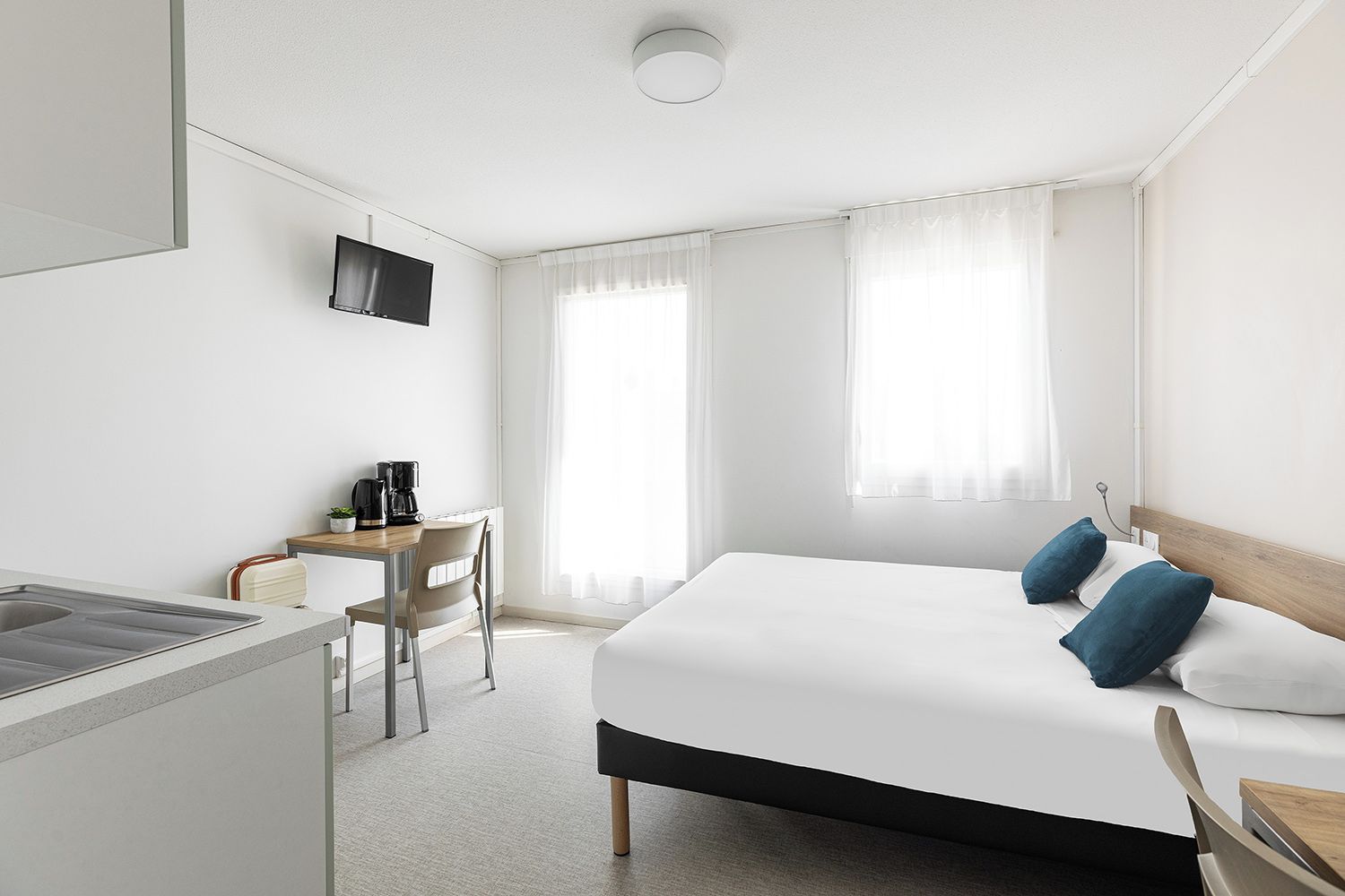 A hotel room with a bed, a desk with a chair, a coffee maker, and a television.