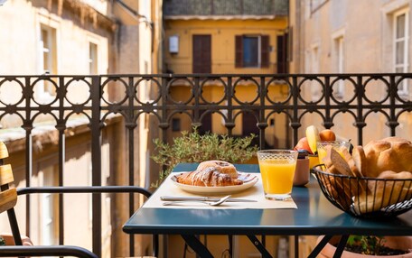 A table with croissants, a glass of orange juice, and a basket of bread on a balcony with a wrought iron railing.