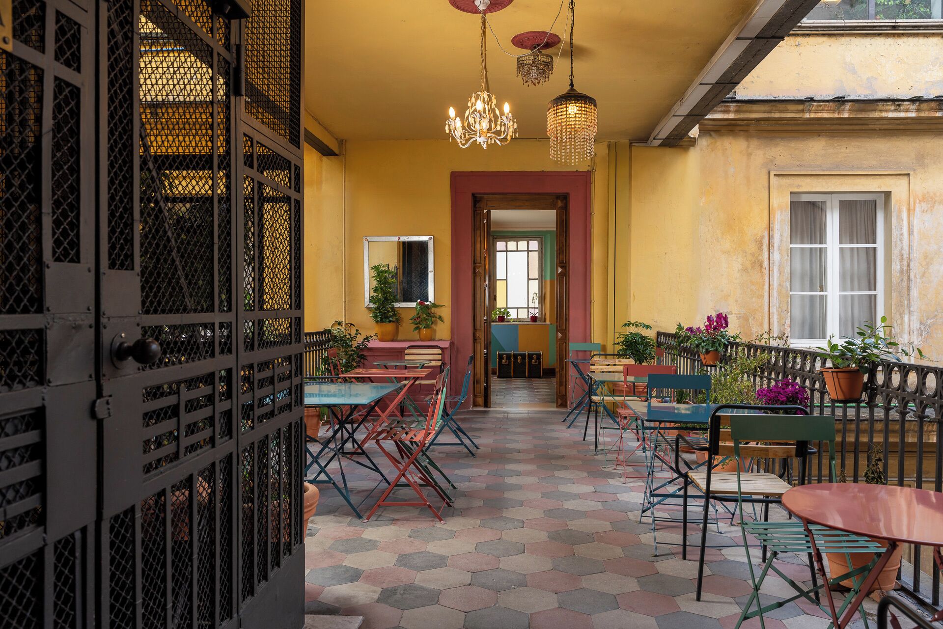 An interior with hexagonal patterned flooring, a central doorway, and a seating area with tables and chairs.