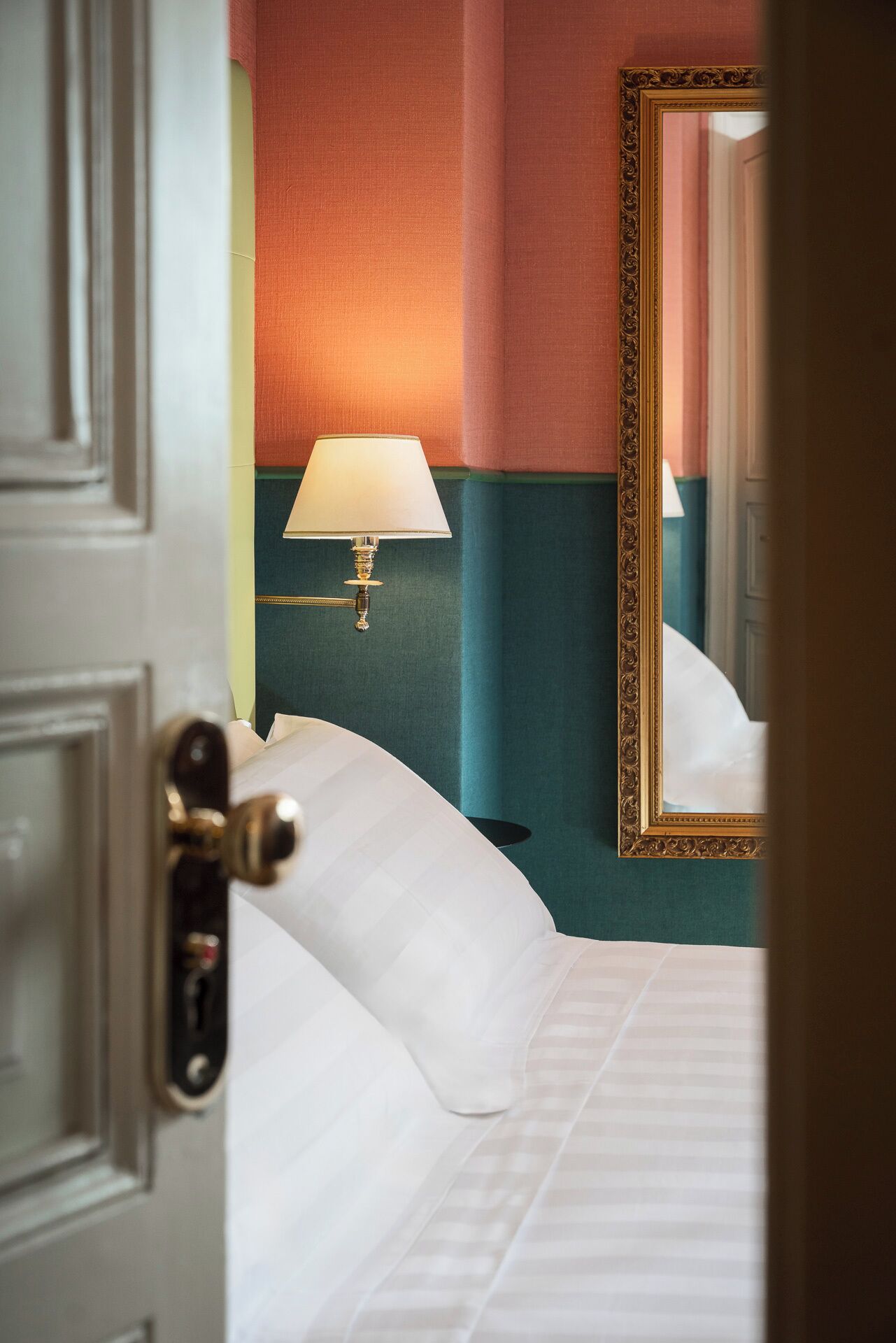 A hotel room with a bed, a nightstand, a lamp, and a mirror.