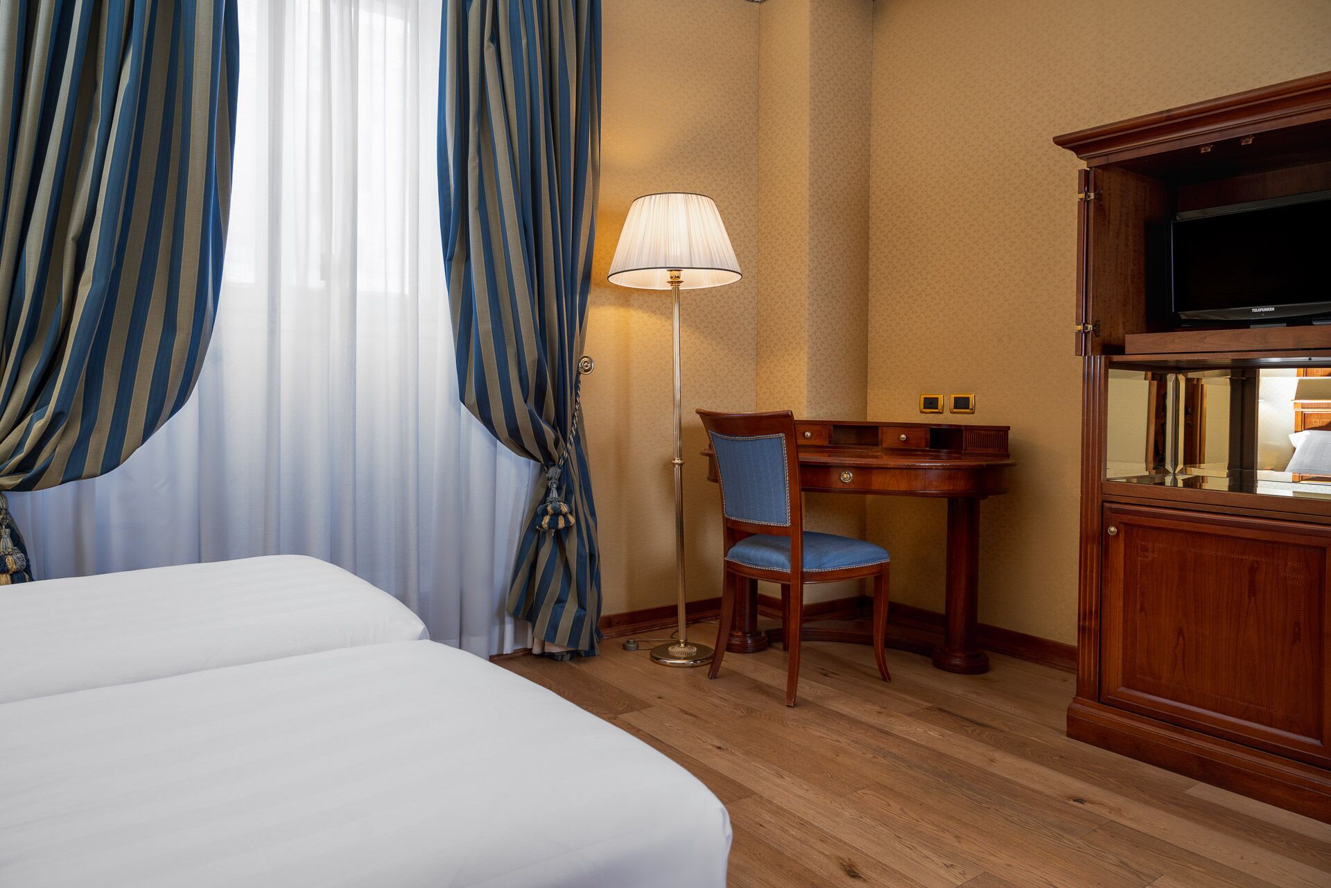 A hotel room with a bed, a desk, a chair, a lamp, and a TV.