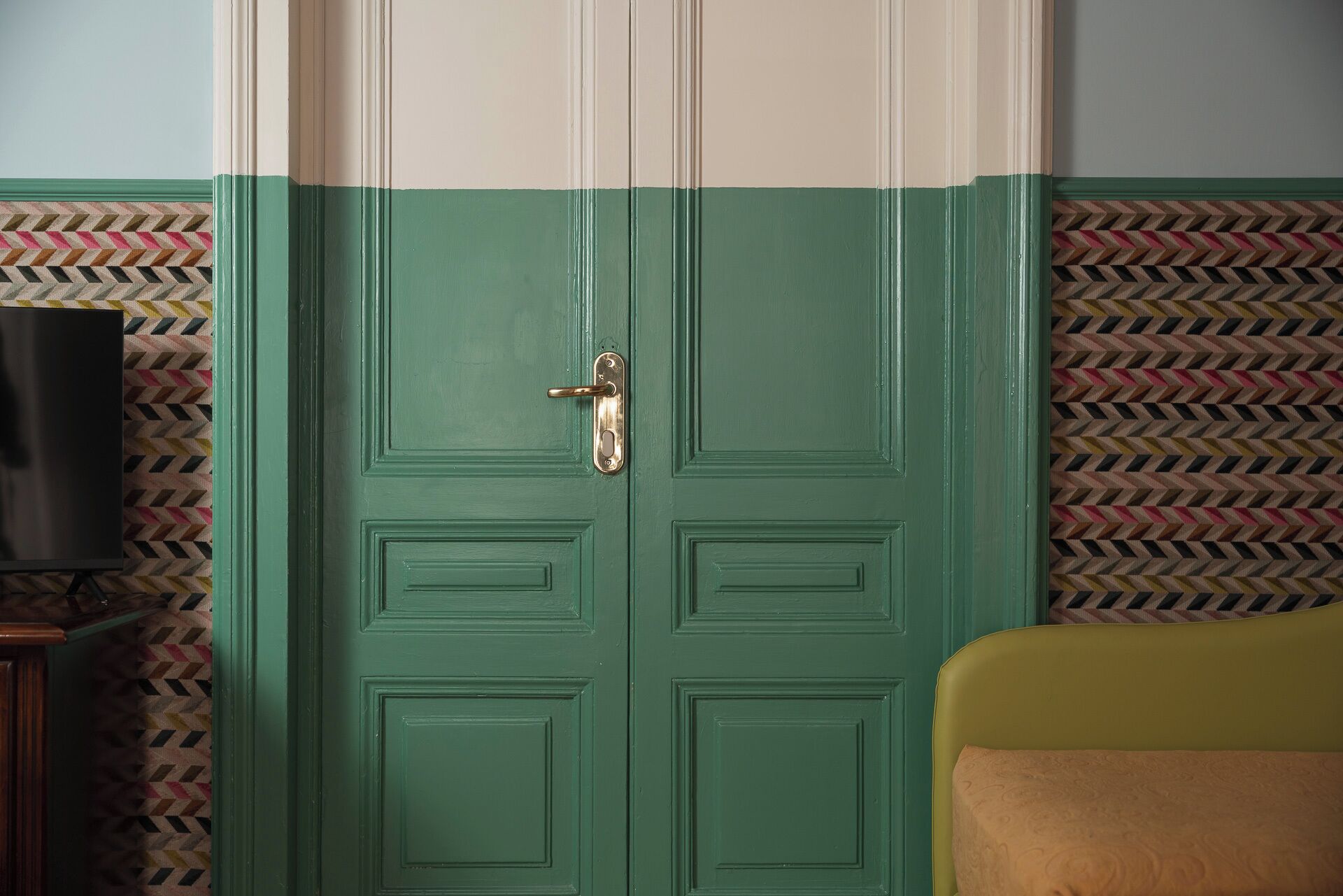 Una habitación con una puerta verde, un televisor a la izquierda y un papel tapiz estampado.