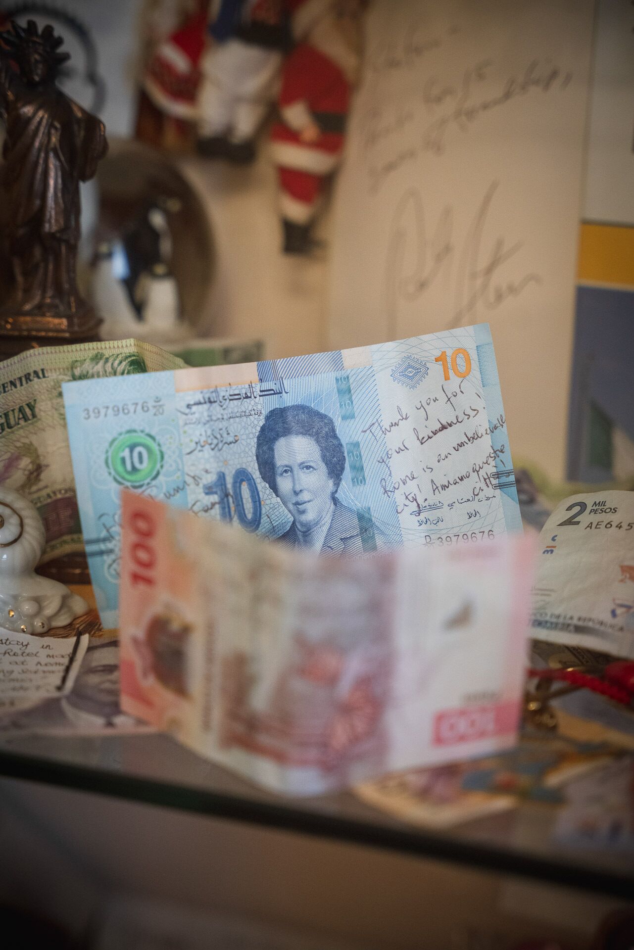 Ein 10-Peso-Schein mit einem Porträt und einer Unterschrift, umgeben von anderen Banknoten und einer Statue.