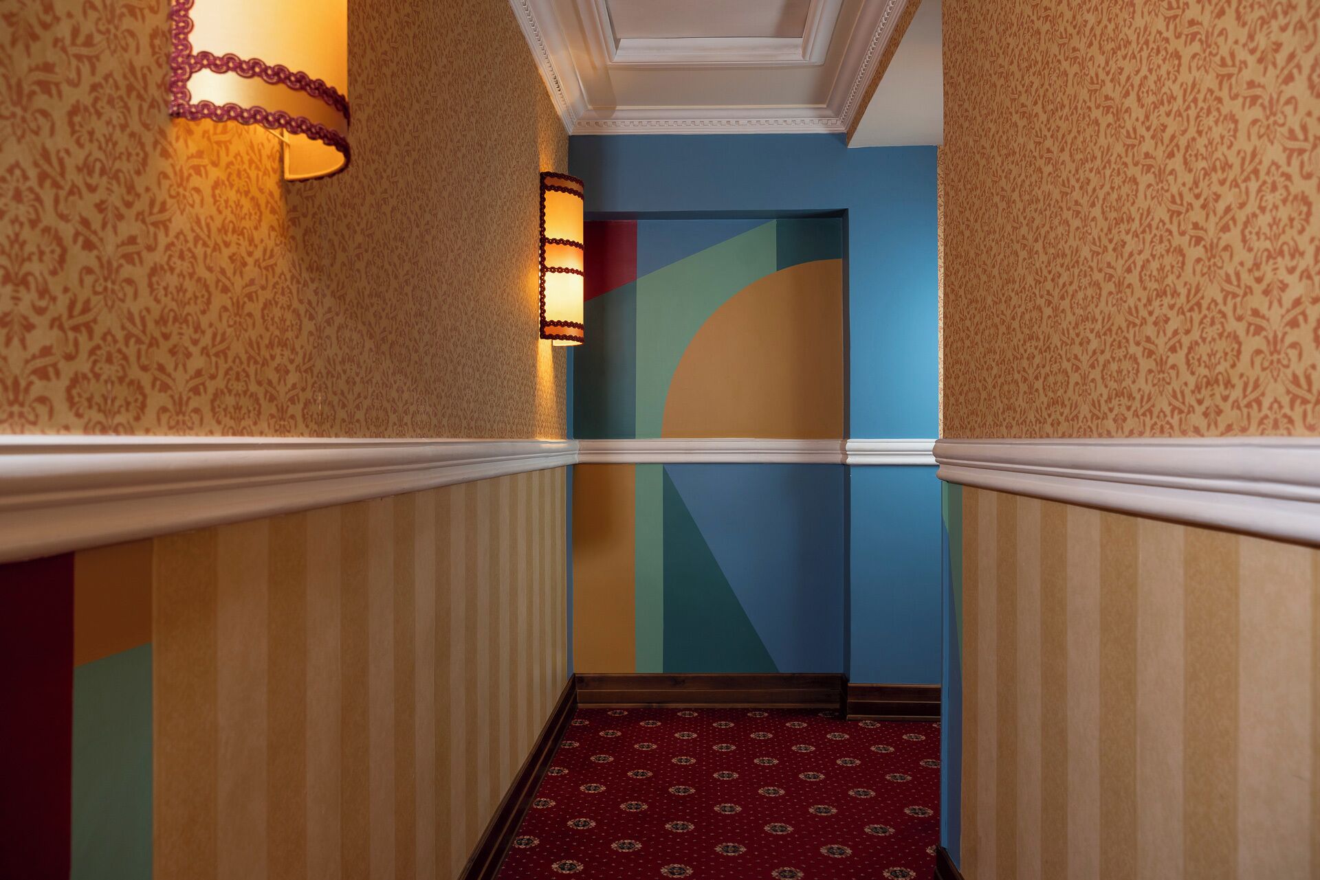 Un pasillo con papel tapiz estampado, alfombra roja y una pared azul de acento.