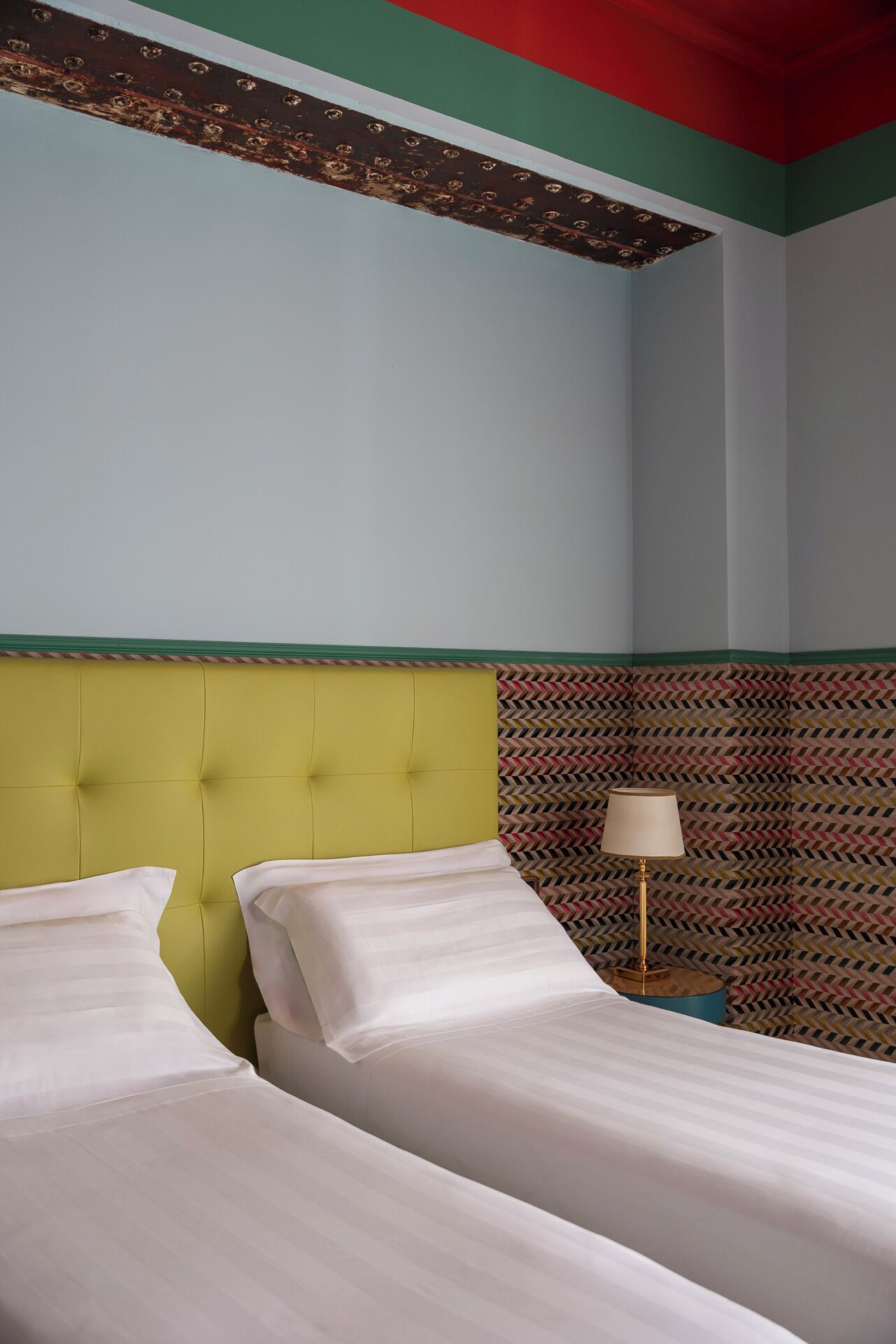 Habitación de hotel con dos camas, cabecero verde, pared estampada y techo rojo.