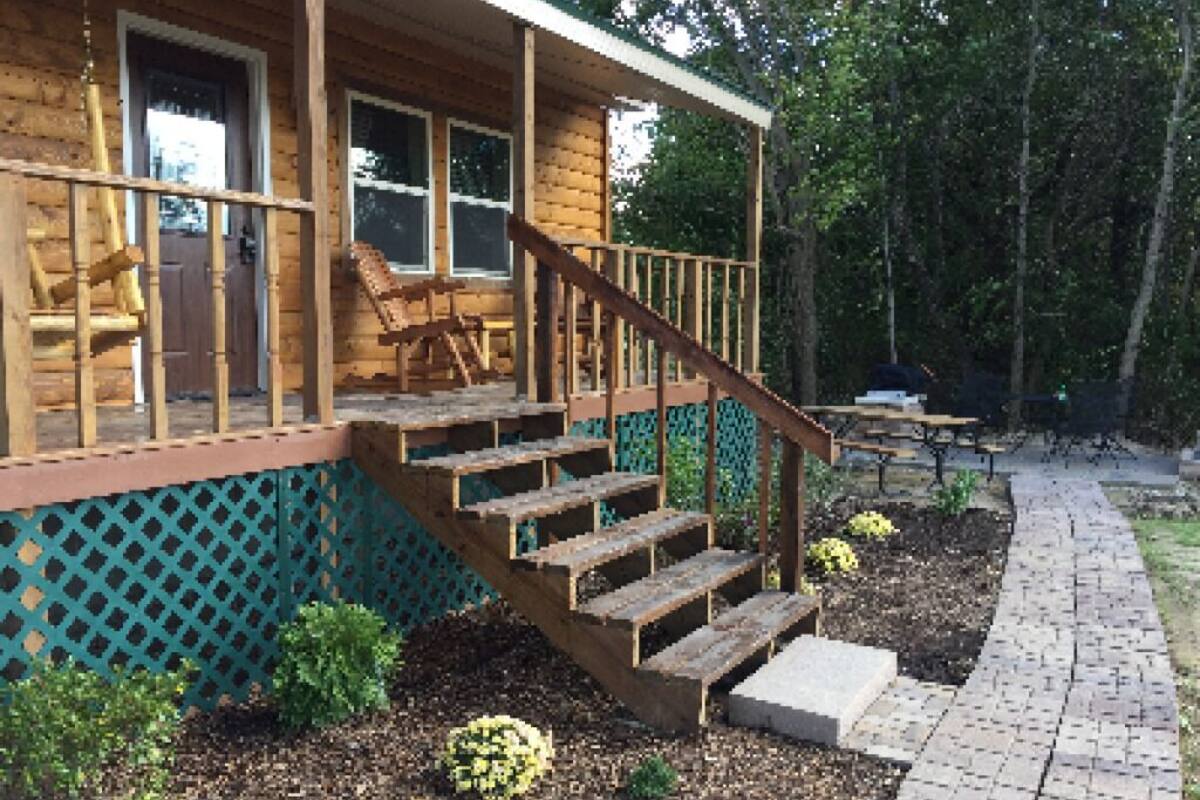 A wooden cabin with a porch, wooden steps, and a fenced garden area.