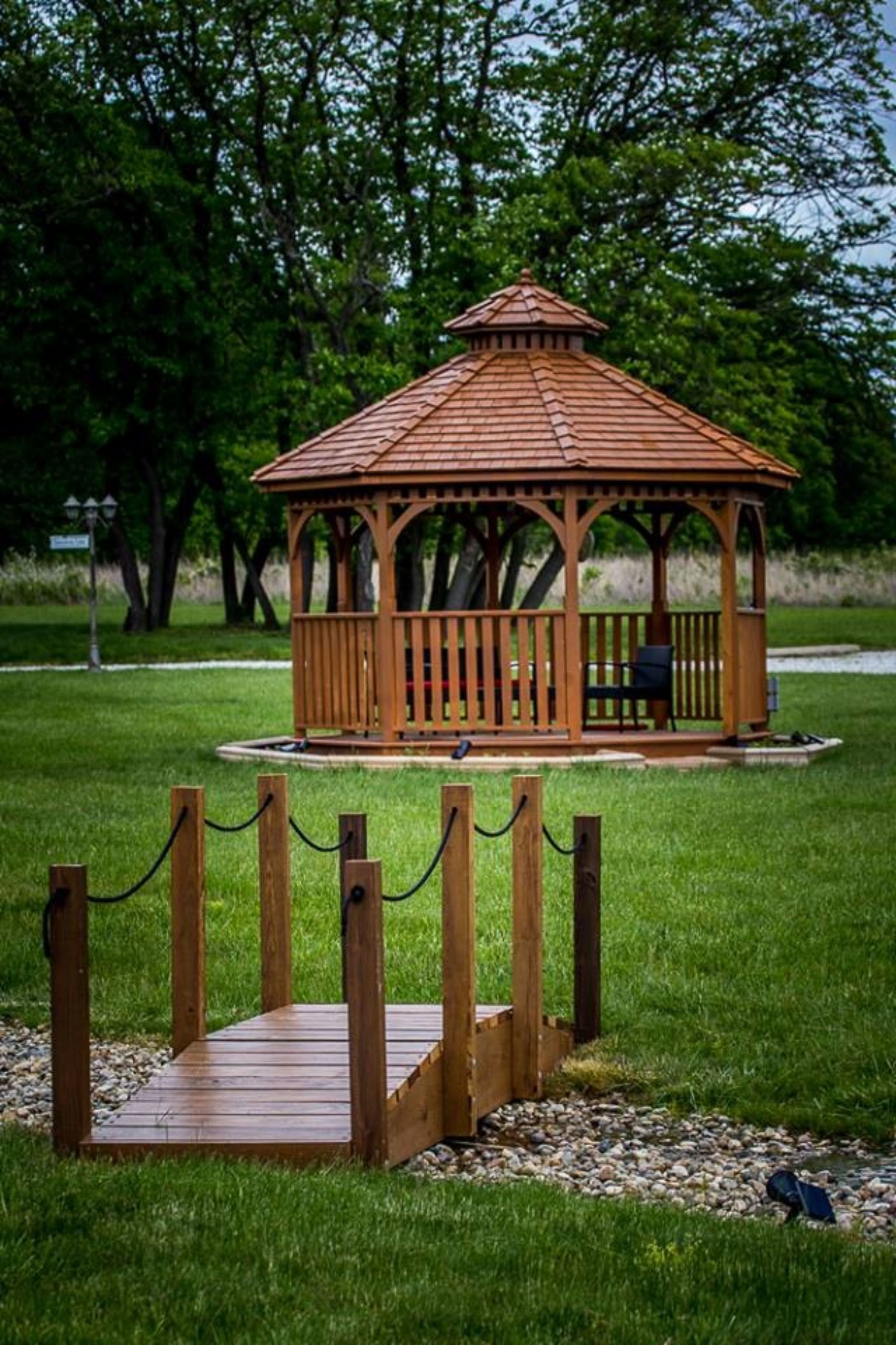 A wooden gazebo with a tiled roof, surrounded by a wooden fence and a gravel path.