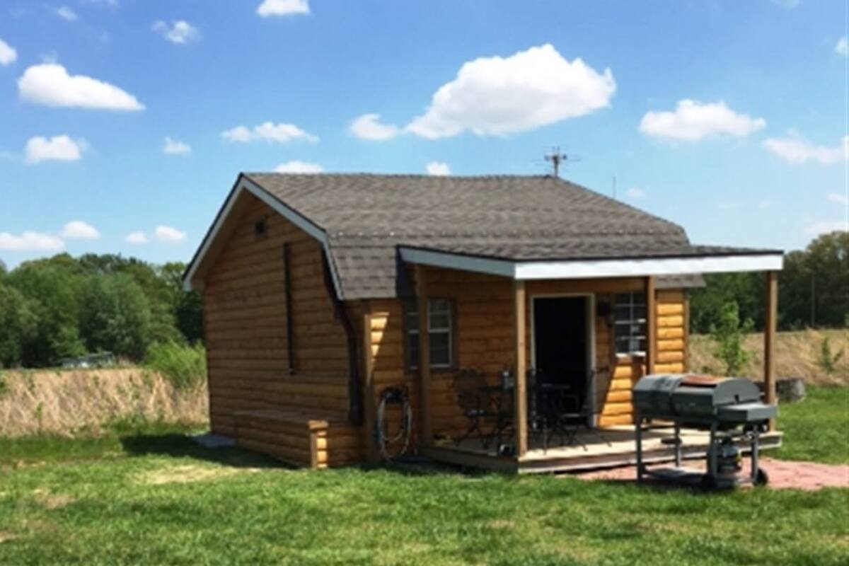 A small wooden cabin with a porch, a grill, and a bicycle.