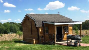 A small wooden cabin with a porch, a grill, and a bicycle.