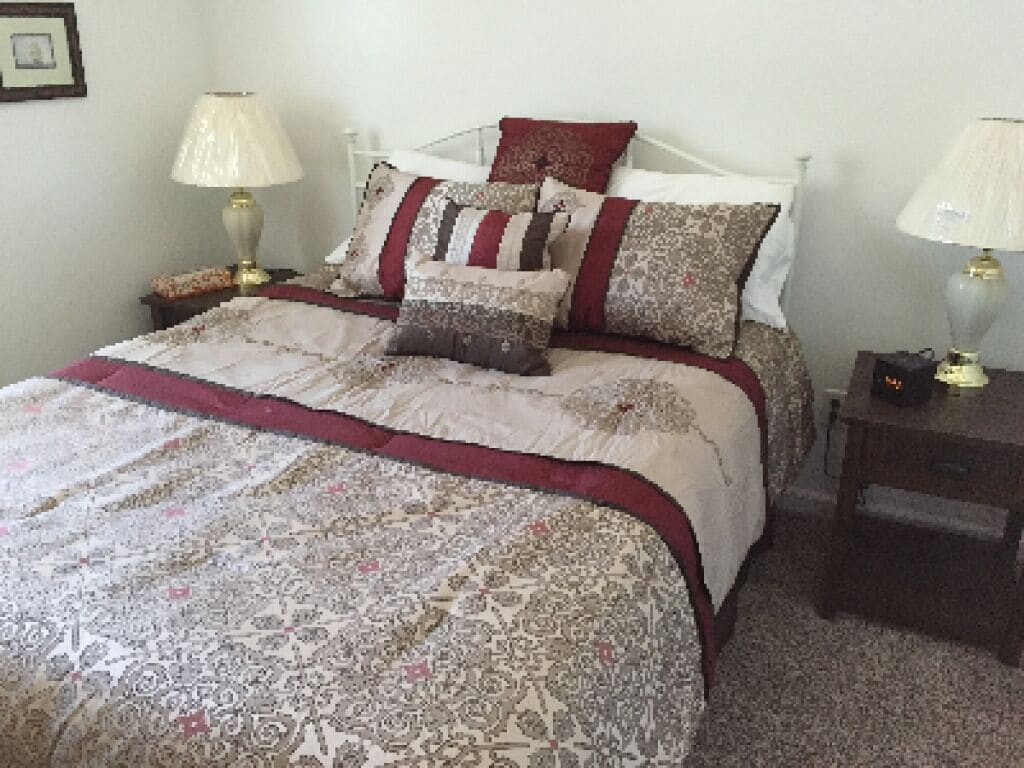 A neatly made bed with patterned bedding and pillows, two bedside lamps, and a small bedside table with a lamp.