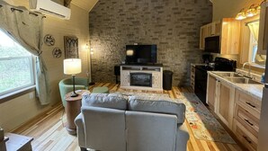Una sala de estar acogedora con una pared de piedra, un televisor de pantalla plana, un sofá y un comedor con armarios de madera y un lavamanos.