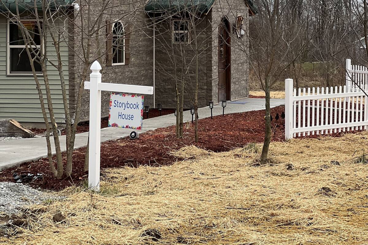 A brick house with a green roof, a white picket fence, and a 'Storagehouse' sign.