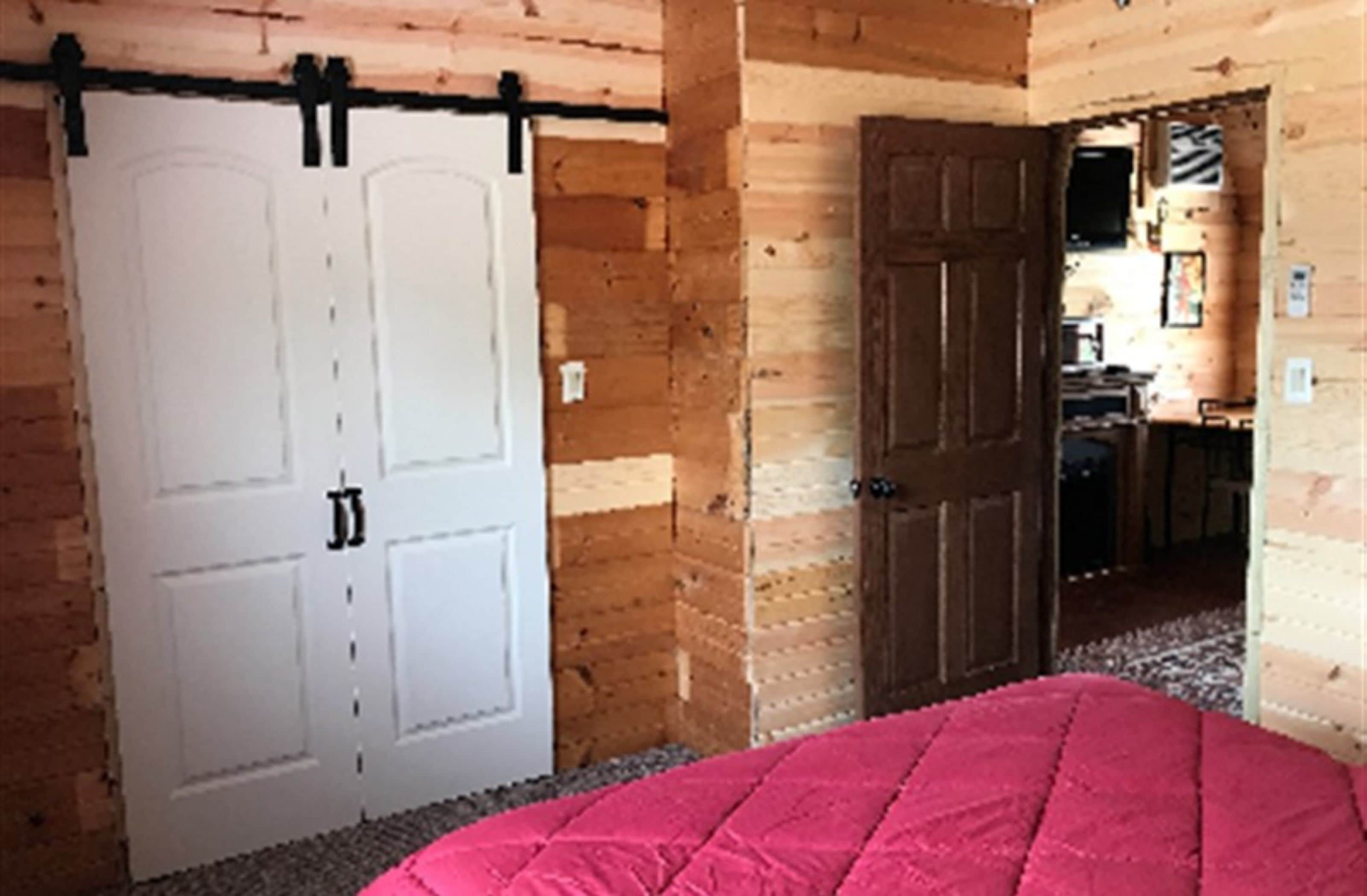 Una habitación con una cama, una puerta blanca y paredes de madera.
