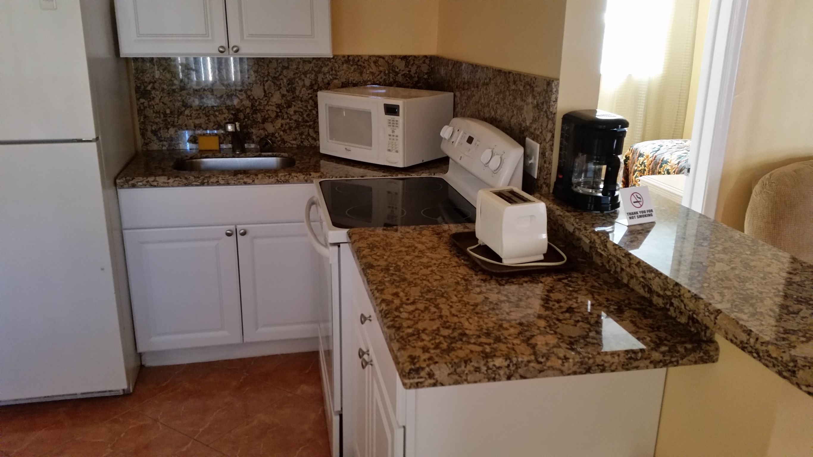 A compact kitchen with white cabinets, a granite countertop, a microwave, a toaster, and a coffee maker.