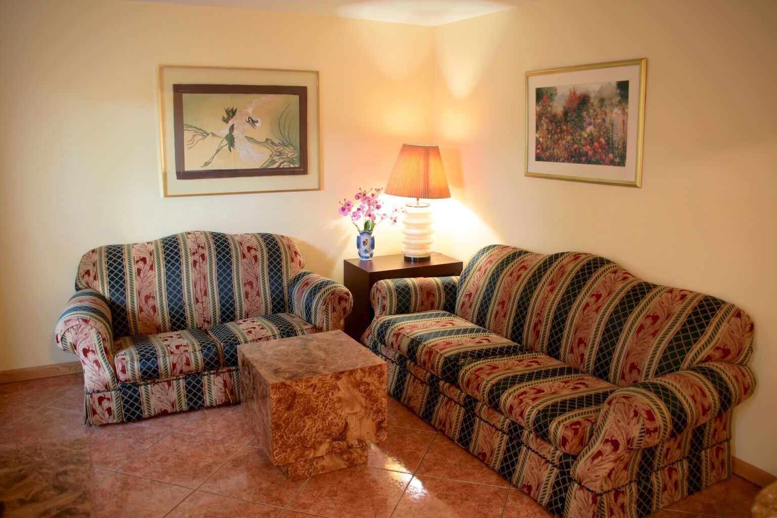 A living room with two patterned sofas, a wooden coffee table, a lamp, and two framed pictures on the walls.