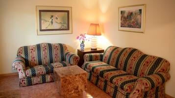 A living room with two patterned sofas, a wooden coffee table, a lamp, and two framed pictures on the walls.