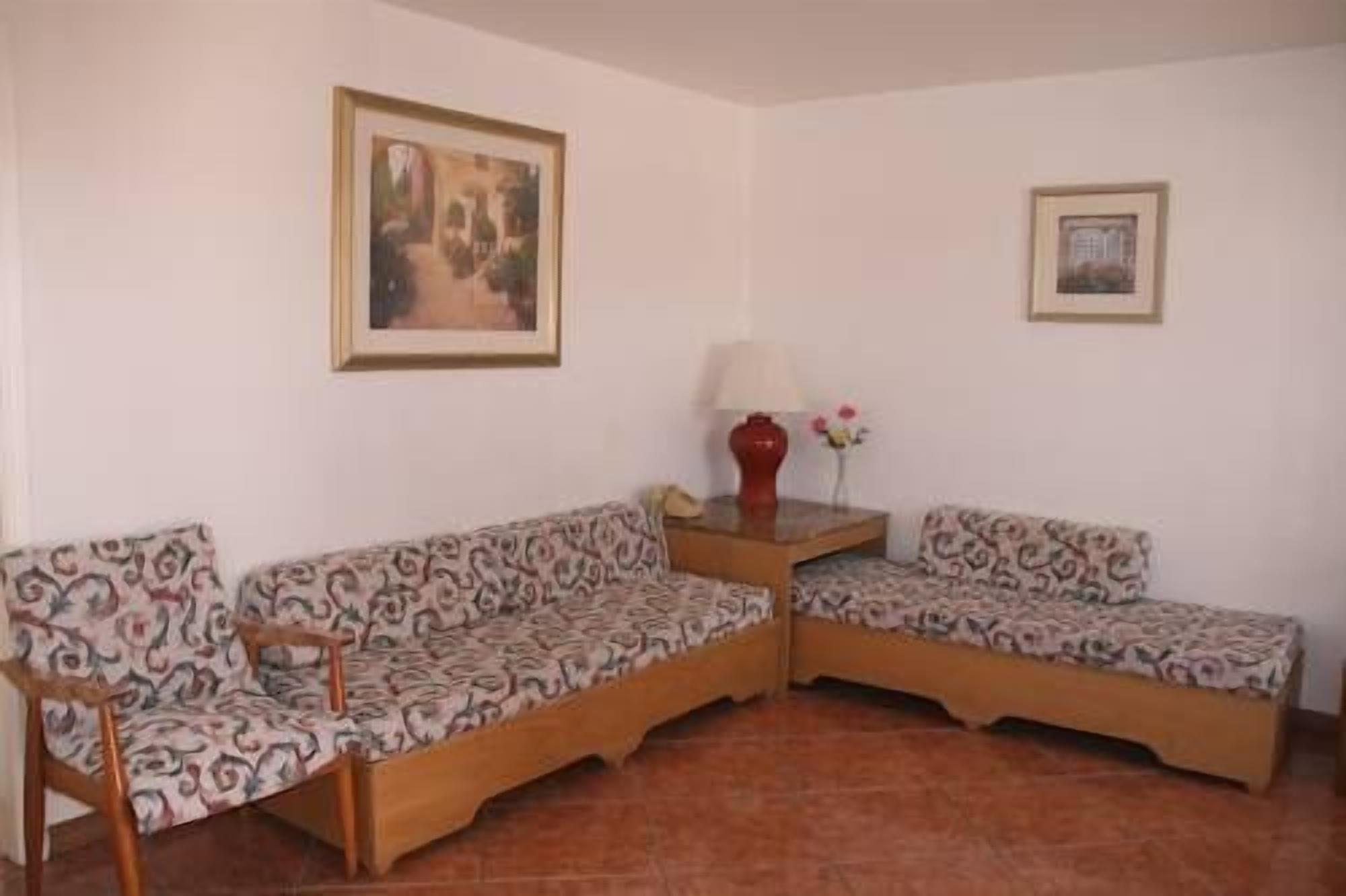 A room with two patterned sofas, a small table with a vase, and two framed pictures on the walls.