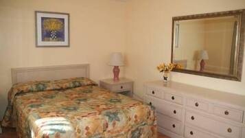 A bedroom with a bed, a nightstand, a dresser, a mirror, and a framed picture on the wall.
