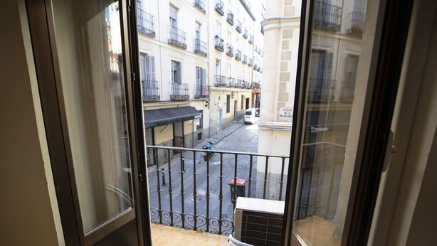 A balcony with a metal railing, a tiled floor, and a view of a street with buildings and a parked scooter. - Hostal MYD Los Perales (Madrid)