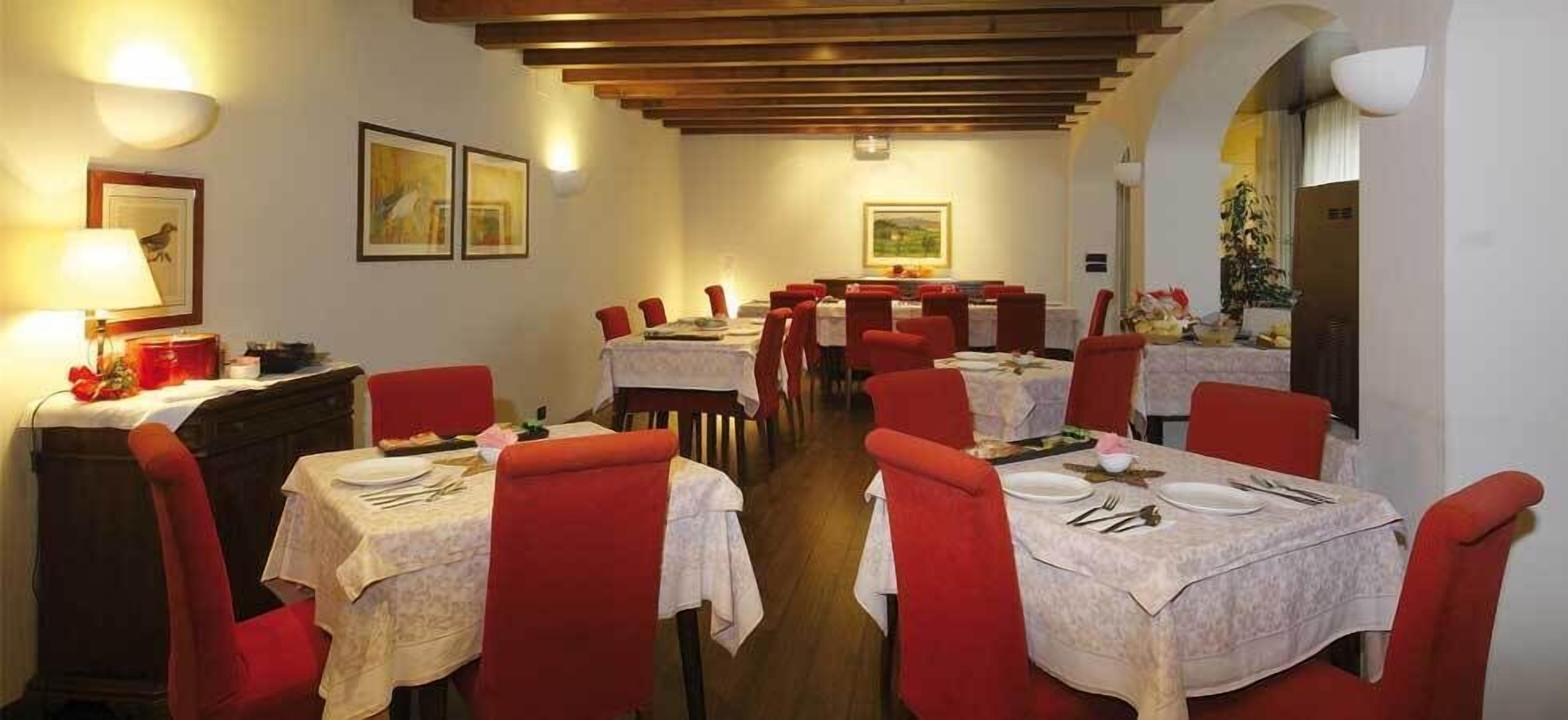 Un comedor con mesas dispuestas para cuatro, sillas tapizadas de rojo y techo de madera.