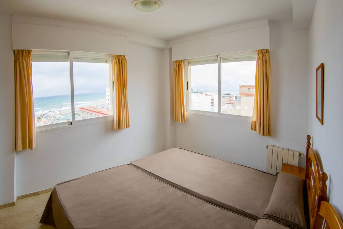 Una habitación con dos ventanas, una cama y un radiador.