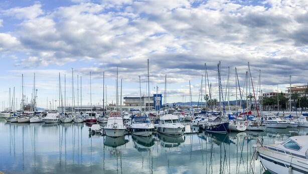 Eine Marina mit zahlreichen vertäuten Booten, ein Gebäude im Hintergrund und ein klarer Himmel.