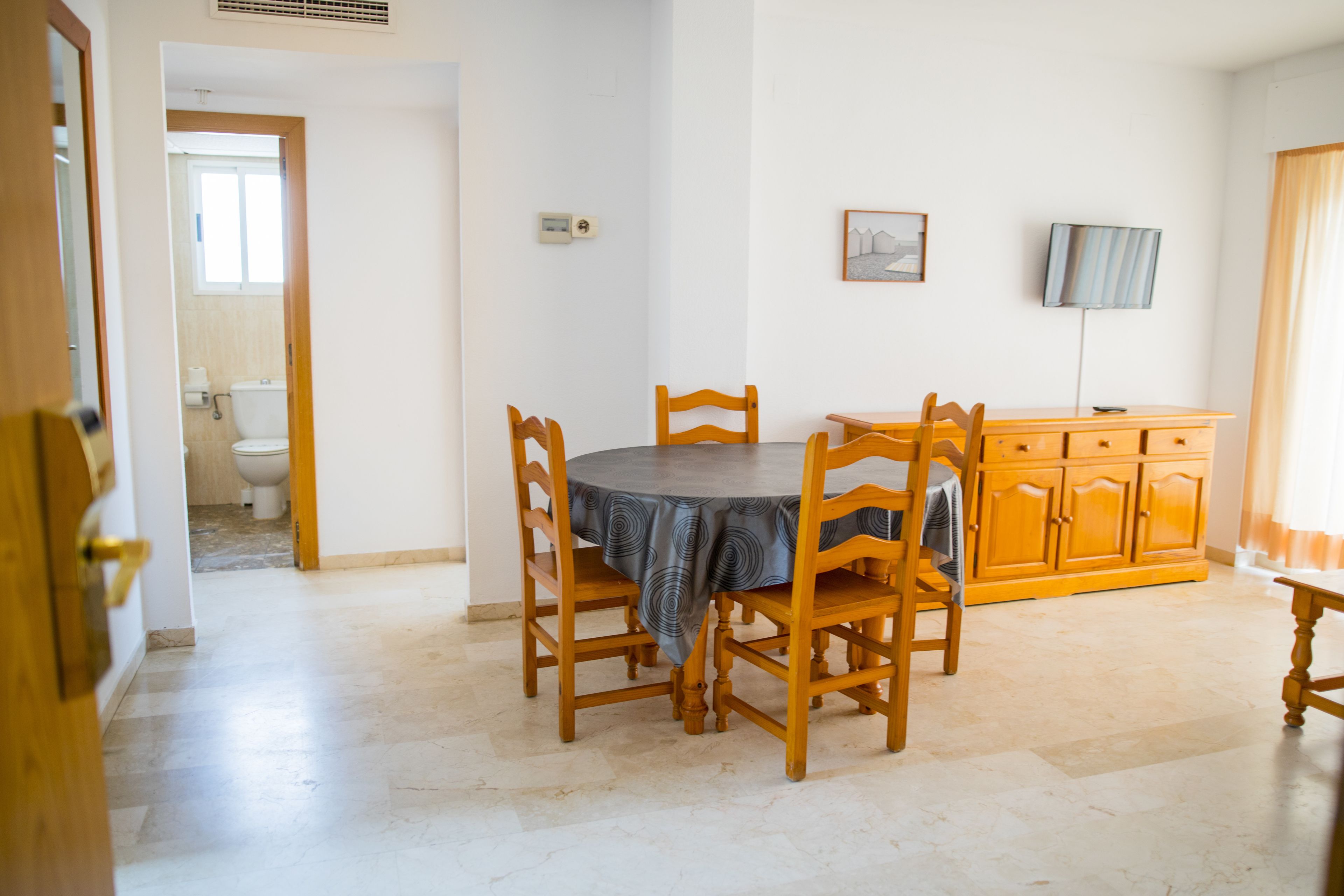 Un coin repas avec une table ronde, des chaises en bois, un buffet et un téléviseur fixé au mur.