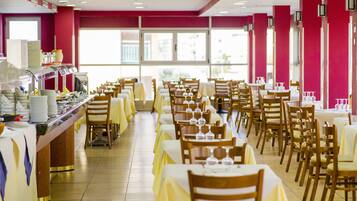 Zona pranzo con diversi tavoli e sedie, un'area buffet con varie pietanze e ampie finestre che lasciano entrare la luce naturale.