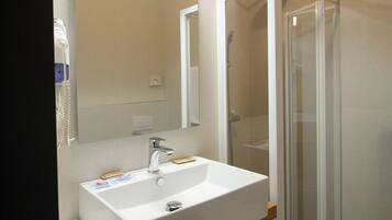 Une salle de bain moderne avec un lavabo blanc, un miroir et une cabine de douche en verre.