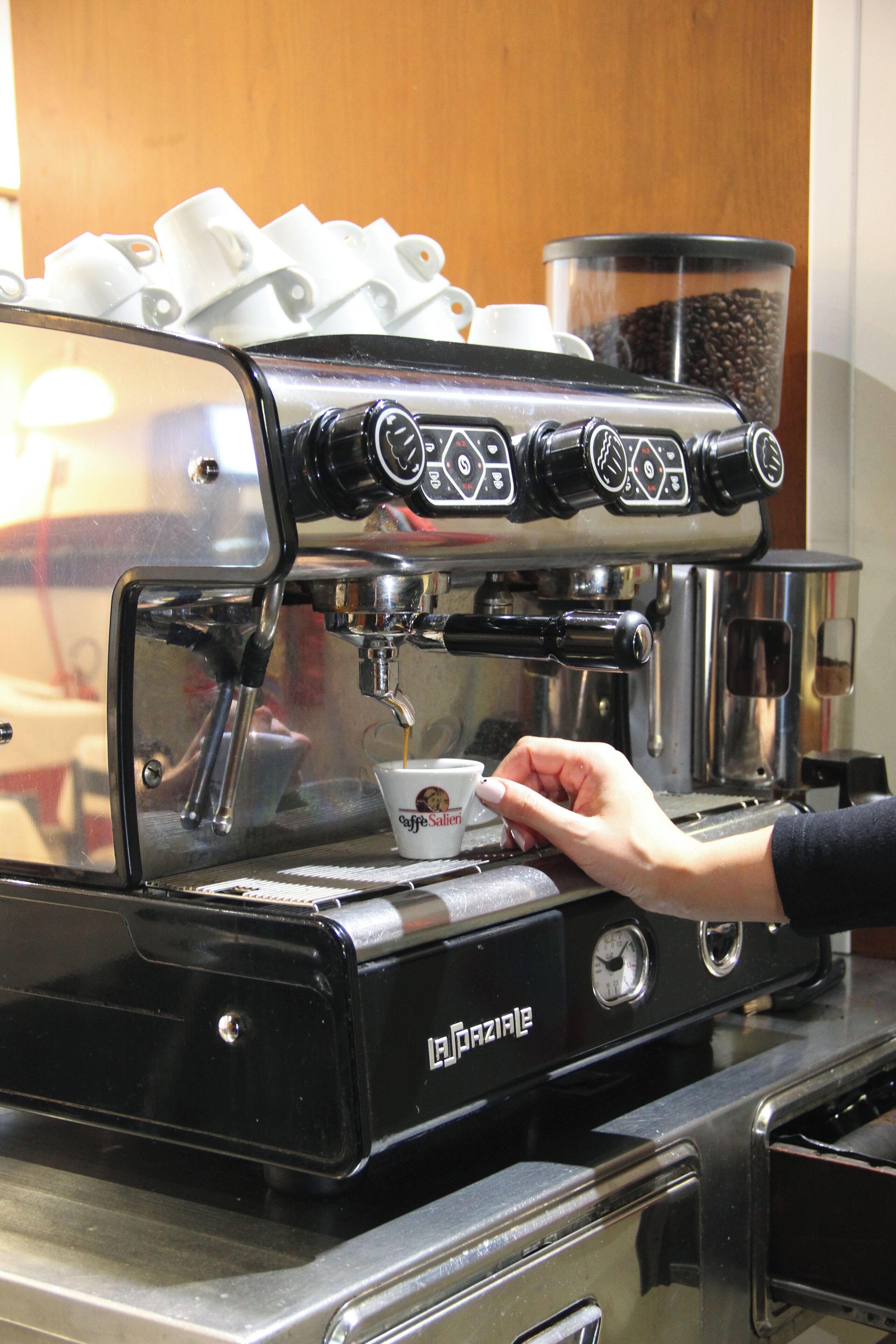 A person operating a La Bazarie branded espresso machine, with a cup of coffee being prepared.