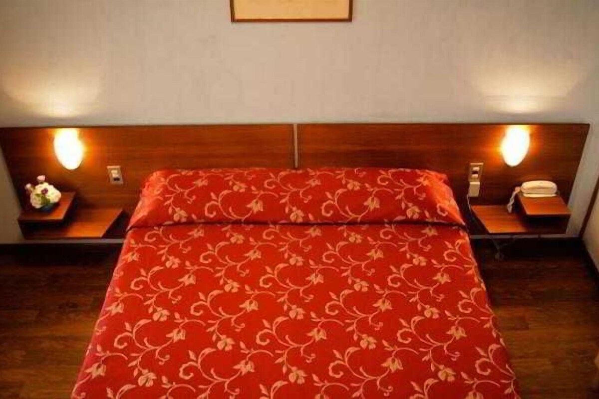 Una habitación de hotel con una cama, dos mesitas de noche y una mesita auxiliar con una lámpara.