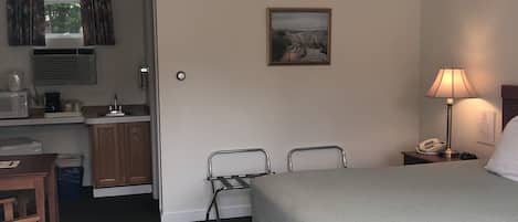 A hotel room with a bed, a desk, a chair, a ceiling fan, a lamp, and a painting on the wall.