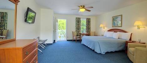 A hotel room with a bed, a dresser, a desk, a chair, a ceiling fan, and a window with curtains.